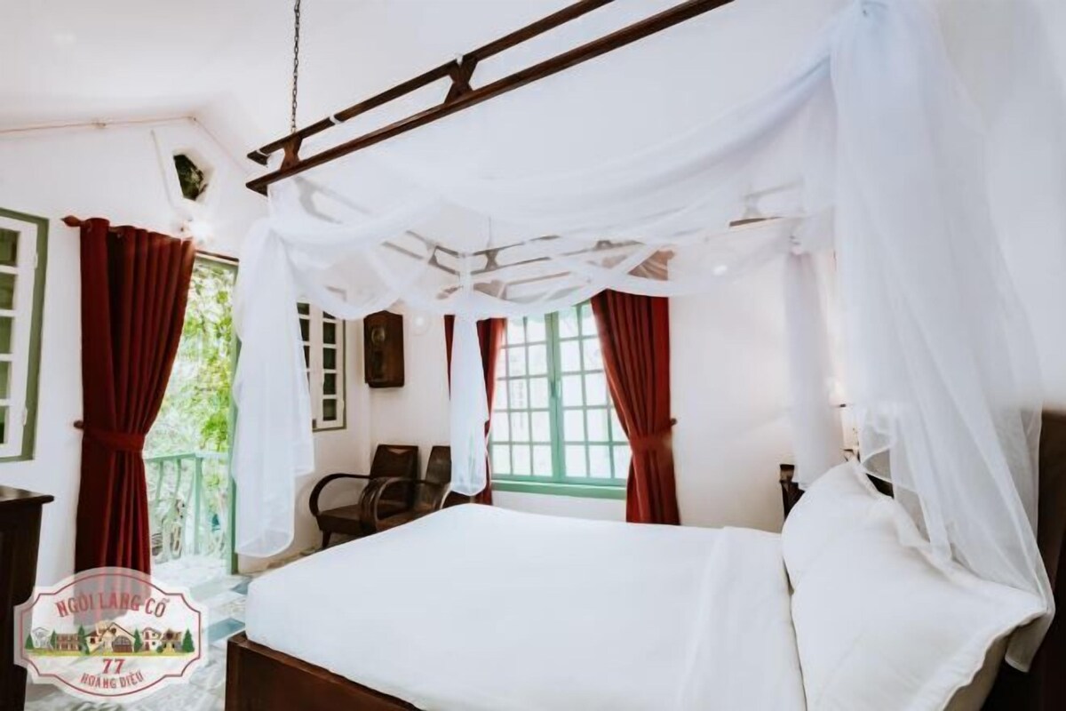 Un dormitorio con cama, una silla, un ventanal con cortinas y un balcón.