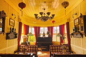 Una habitación con un piano, cortinas rojas y un candelabro.