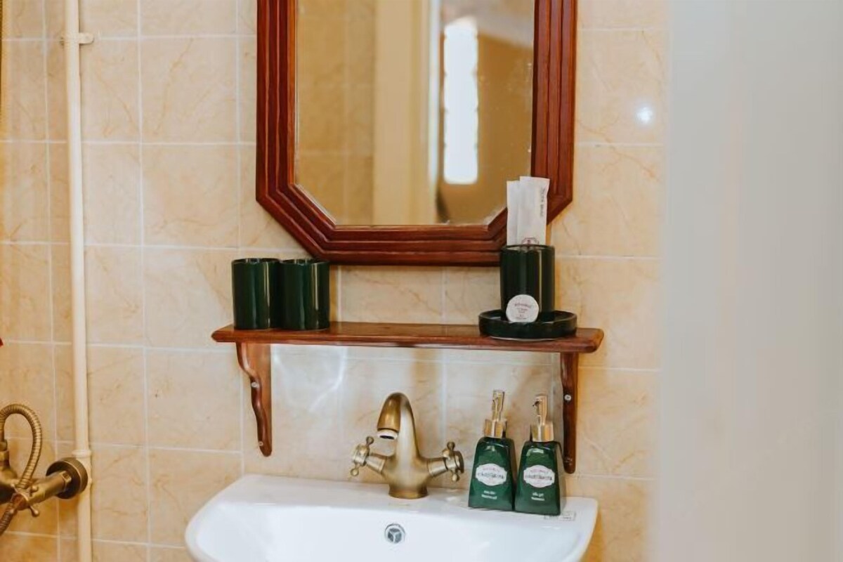 Un baño con un estante de madera que sostiene artículos de aseo, un grifo dorado y un espejo sobre el lavamanos.