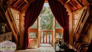 Un intérieur en bois avec un balcon, des rideaux rouges et une vue sur la verdure environnante.