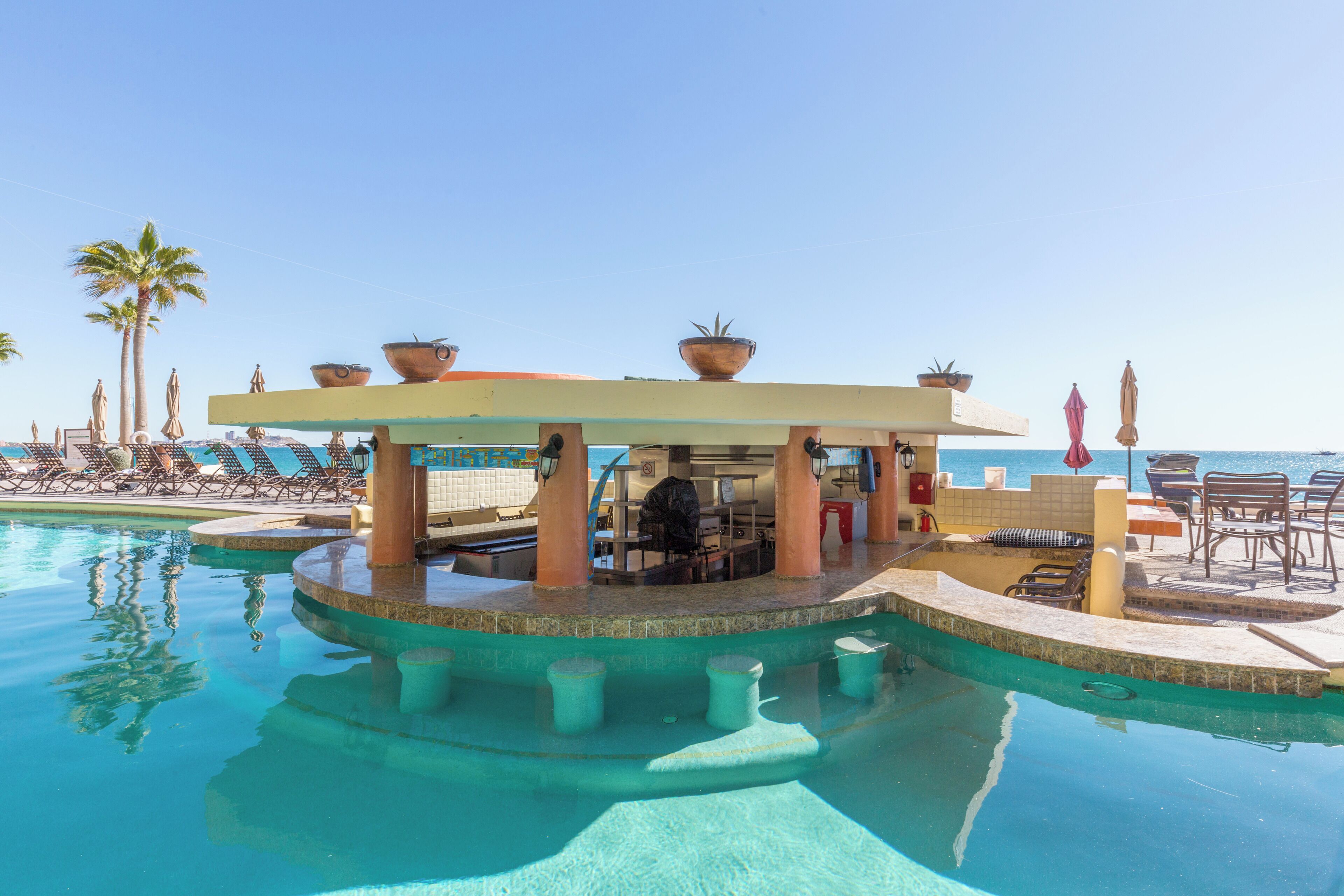 A pool area with lounge chairs, a bar, and a view of the ocean.