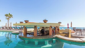 A pool area with lounge chairs, a bar, and a view of the ocean.