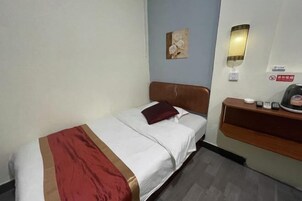 Una habitación de hotel con cama, mesita de noche, lámpara de pared, un cuadro y un cartel.