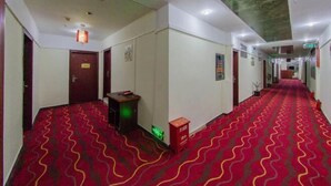 Un couloir d’hôtel avec un tapis rouge à motifs, des portes, un petit bureau et une poubelle.