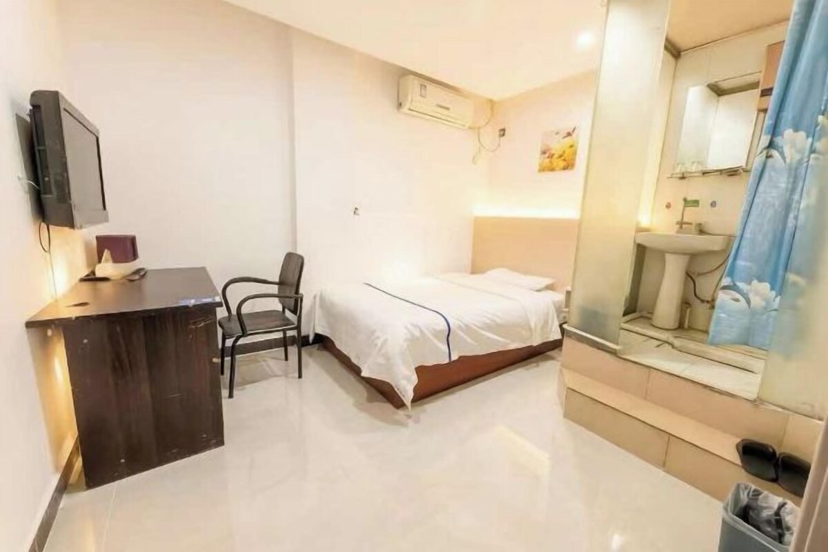 Habitación de hotel con cama, escritorio, silla, televisor y baño con lavabo y espejo.