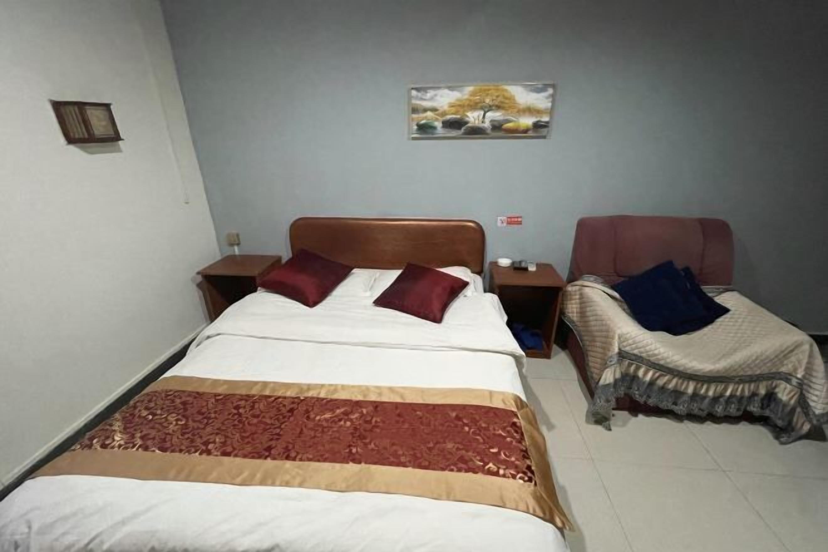 A single bed with a patterned bedspread, a nightstand, a bedside table, and a wall-mounted picture.