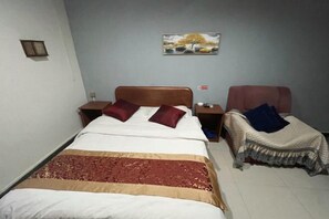 Un lit simple avec une couvre-lit à motifs, une table de chevet et une petite table à poser près du lit, ainsi qu’un tableau accroché au mur.