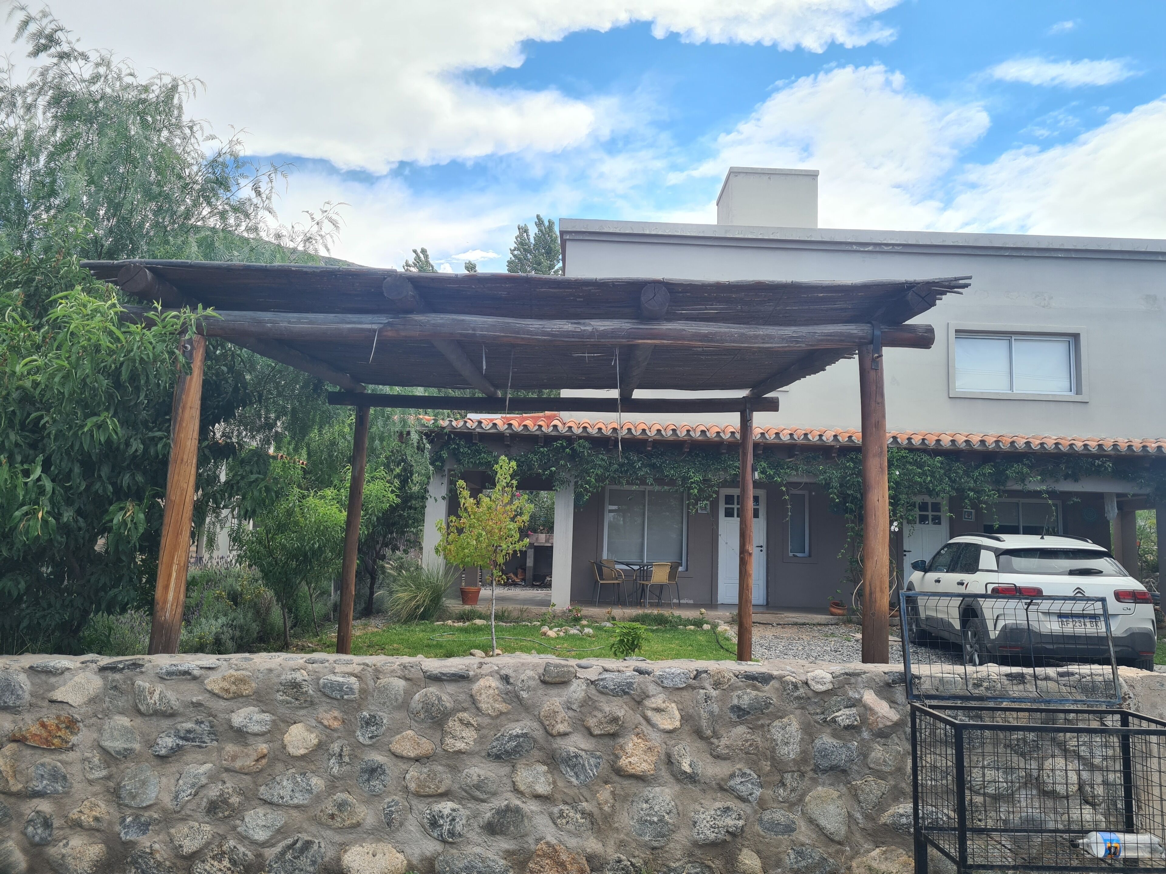 A house with a stone wall, a covered patio, and a parked car.