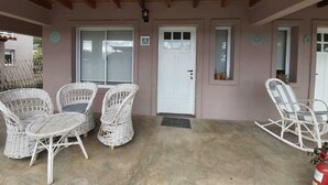 Un patio techado con sillas de mimbre, una puerta blanca y una pequeña planta en maceta.