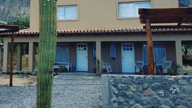 Un edificio moderno de dos pisos con techo plano, un muro de piedra en primer plano y un cactus grande al fondo.