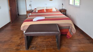 Un dormitorio con techo de madera, una cama con colcha a rayas, un banco, un ventilador de techo y una ventana con vistas.
