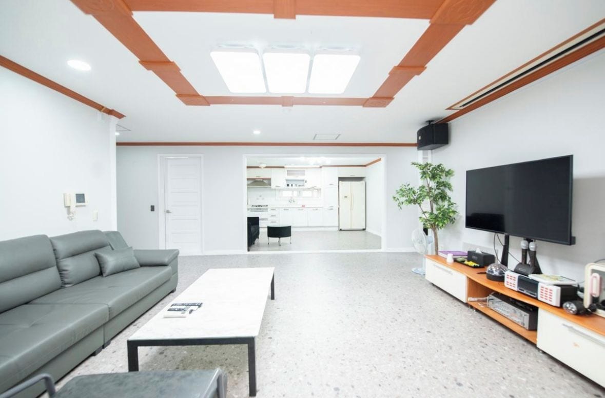 Una sala moderna con un sofá, una mesa de centro, un televisor de pantalla plana y una cocina al fondo.