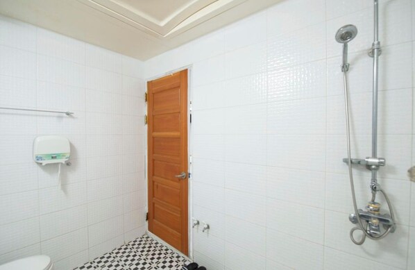 A bathroom with white tiled walls, a wooden door, a white toilet, and a shower with a handheld showerhead. - SongJeong coco hotel (Busan)