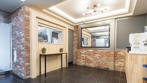 A modern lobby with a brick accent wall, a reception desk, a large mirror, and a ceiling light fixture. - SongJeong coco hotel (Busan)