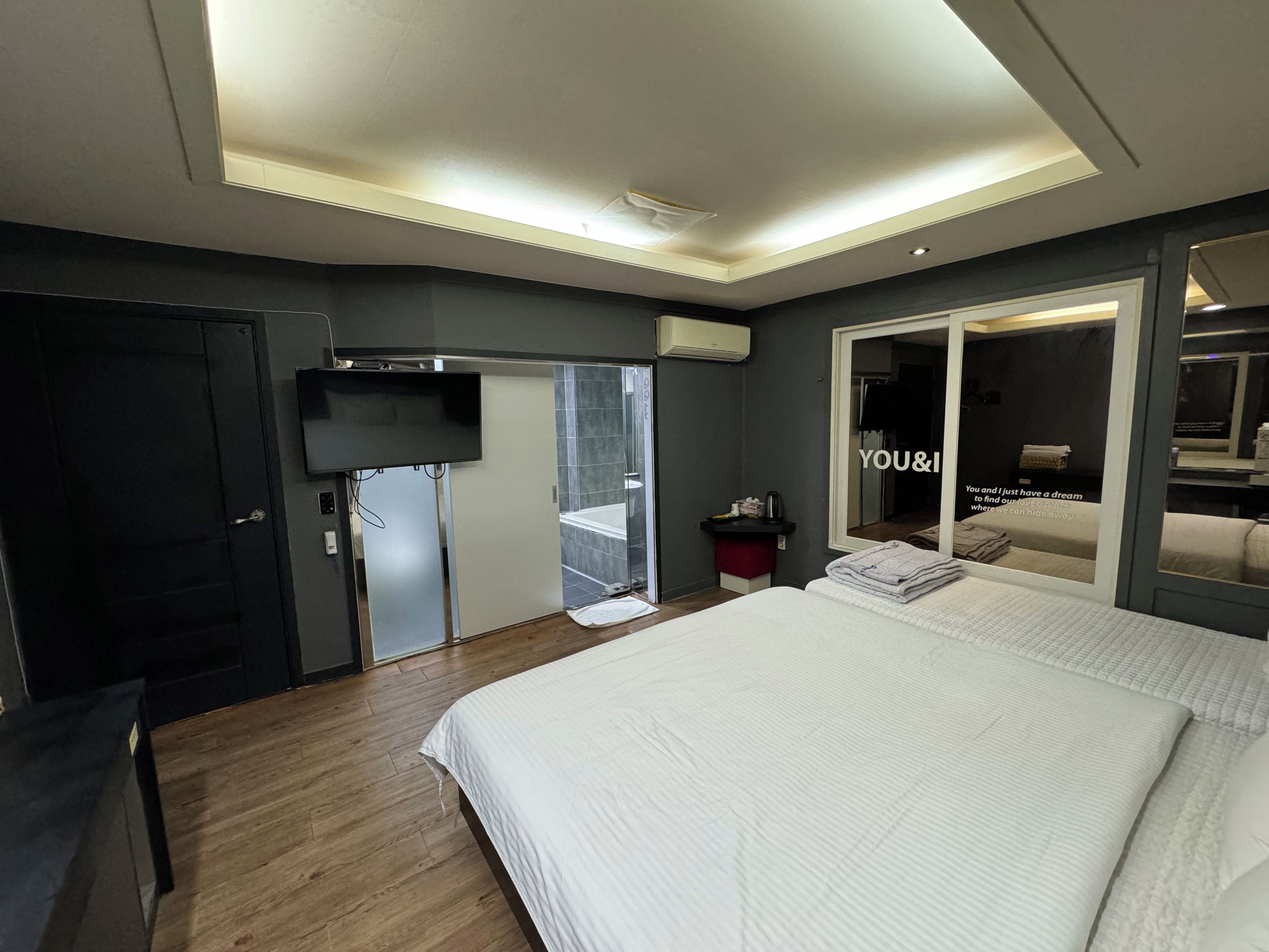 Une chambre d’hôtel moderne dotée d’un grand lit, d’un téléviseur à écran plat, d’une porte coulissante donnant sur un balcon et d’un miroir qui reflète la pièce.