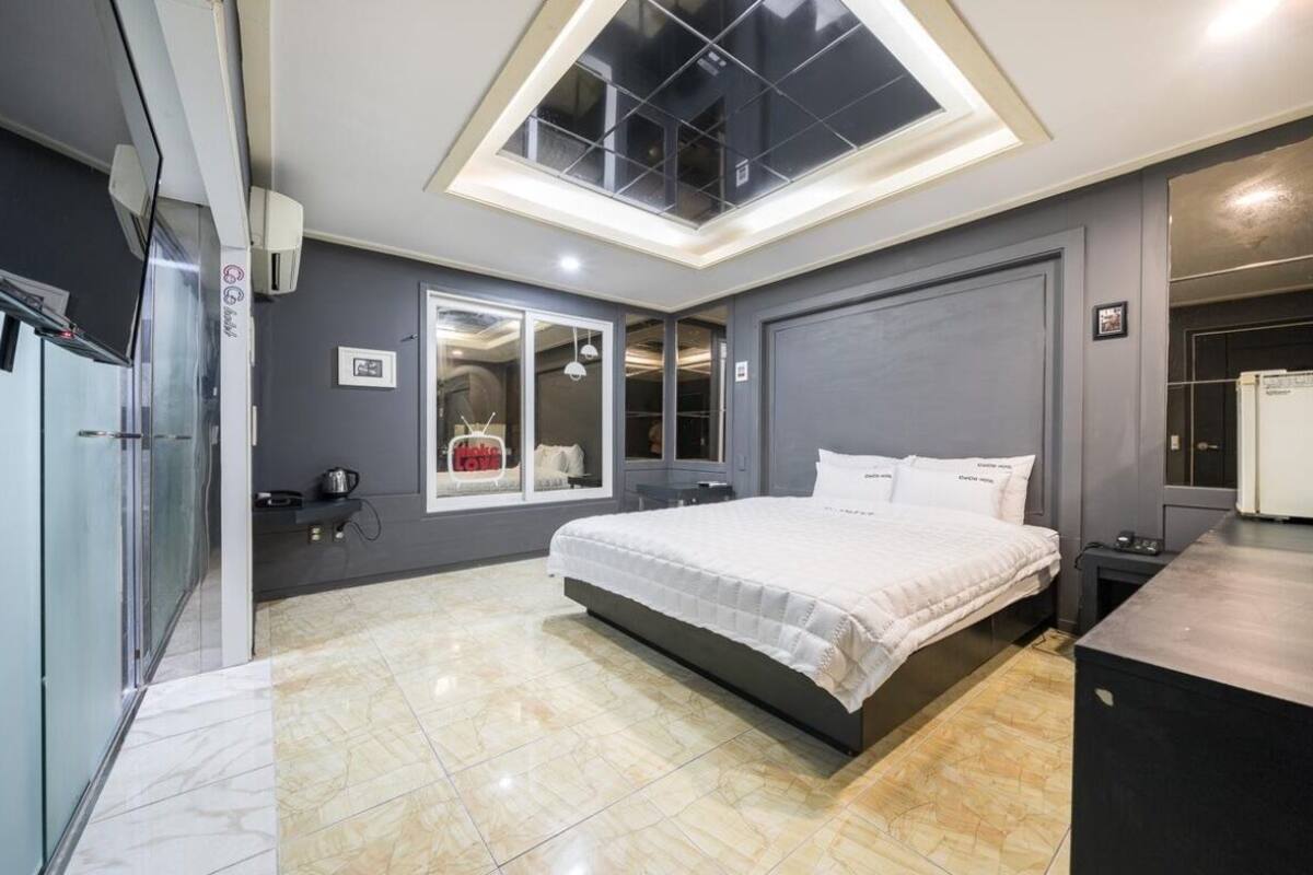 A modern bedroom with a large bed, a skylight, a built-in wardrobe, and a small kitchenette.