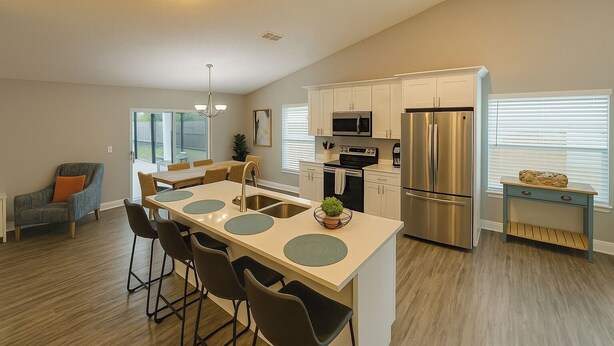 A modern kitchen with a central island, stainless steel appliances, and a dining area with a casual seating arrangement. - Disney-Area 4BR | Pool + Patio (Kissimmee)