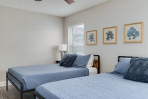 Une chambre avec deux lits, une fenêtre avec des stores et trois œuvres d’art encadrées accrochées au mur.