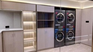 A modern laundry room with two wall-mounted washing machines and a wooden cabinet with shelves. - Ketai Boutique Hotel (Shaoxing Keqiao Oriental Landscape Park) (Shaoxing)