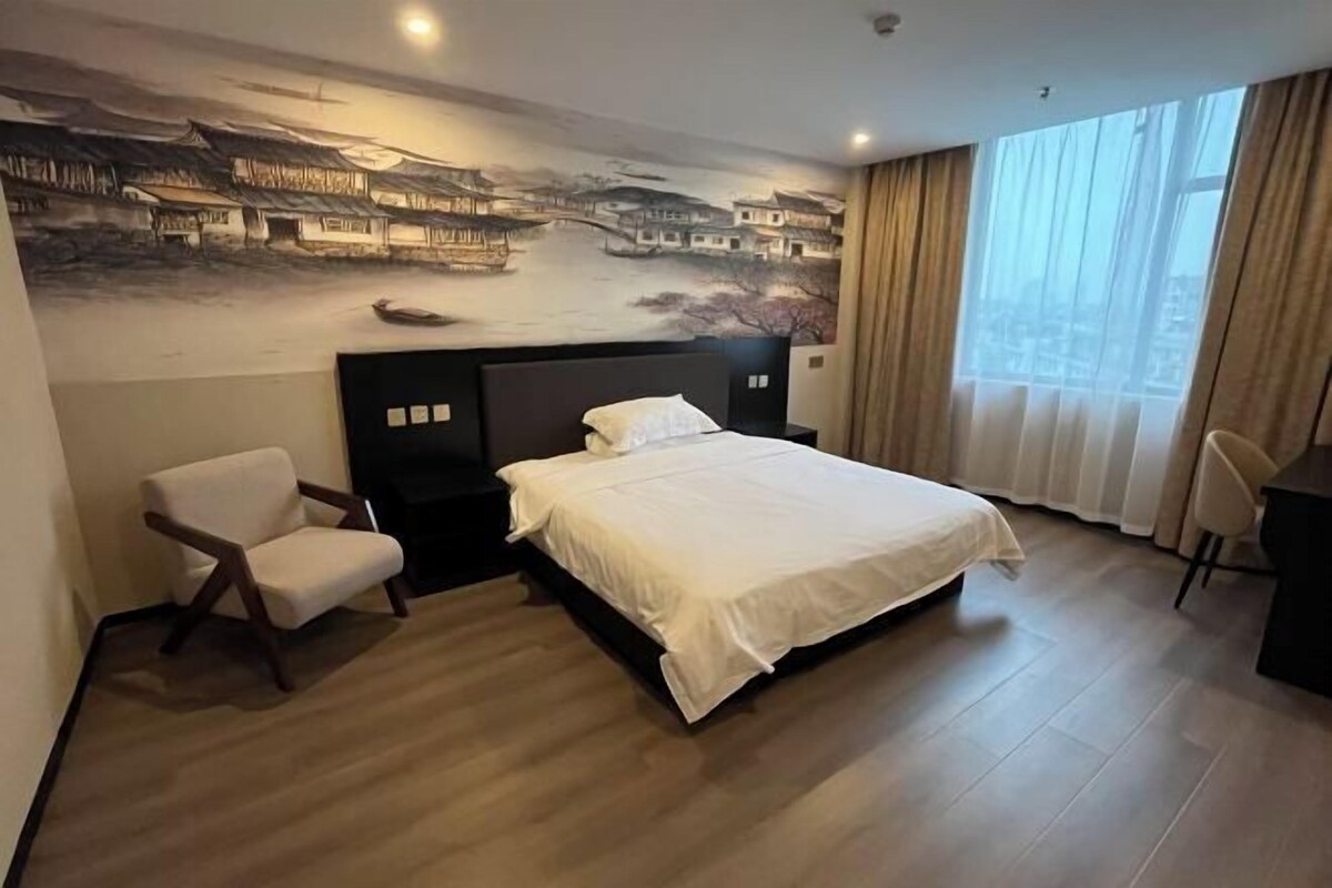 Une chambre d’hôtel avec un grand lit, une chaise, un bureau et une fresque représentant une scène traditionnelle sur le mur.