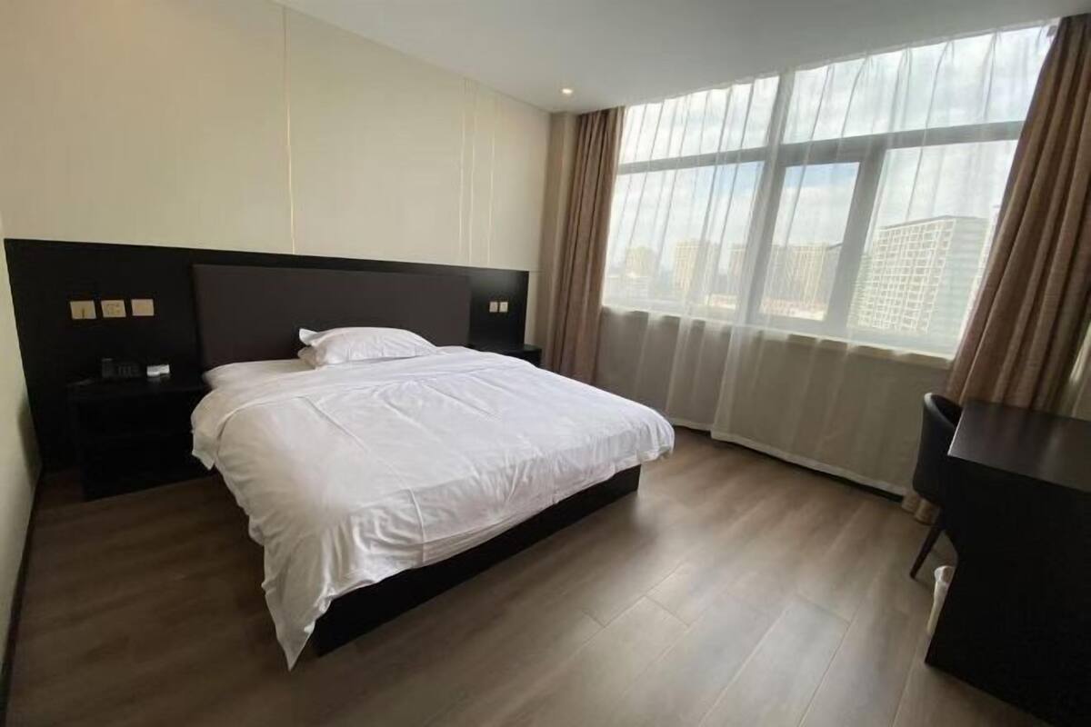 Une chambre d’hôtel avec un grand lit, une table de chevet, un bureau et une fenêtre avec des rideaux.