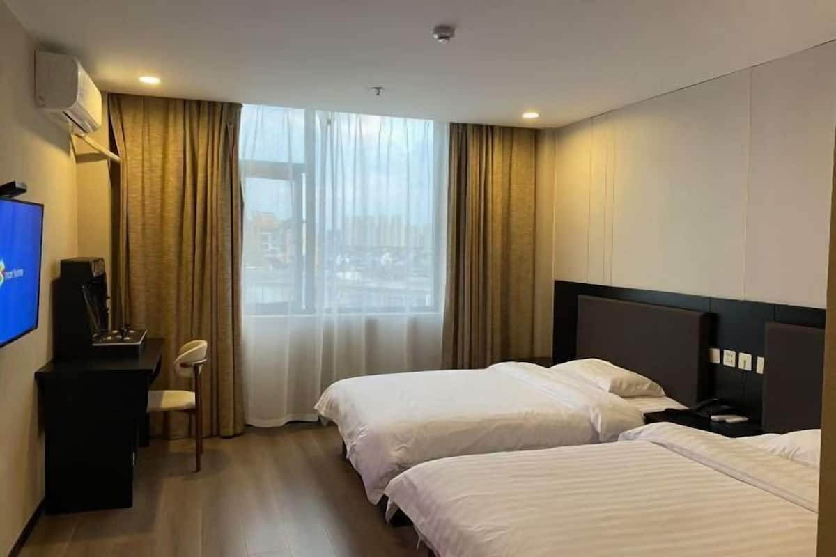 Une chambre d’hôtel avec deux lits, un bureau avec une chaise, une télévision et une fenêtre avec des rideaux.