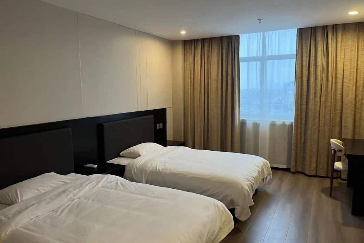 Une chambre d’hôtel avec deux lits, un bureau et une fenêtre avec des rideaux.