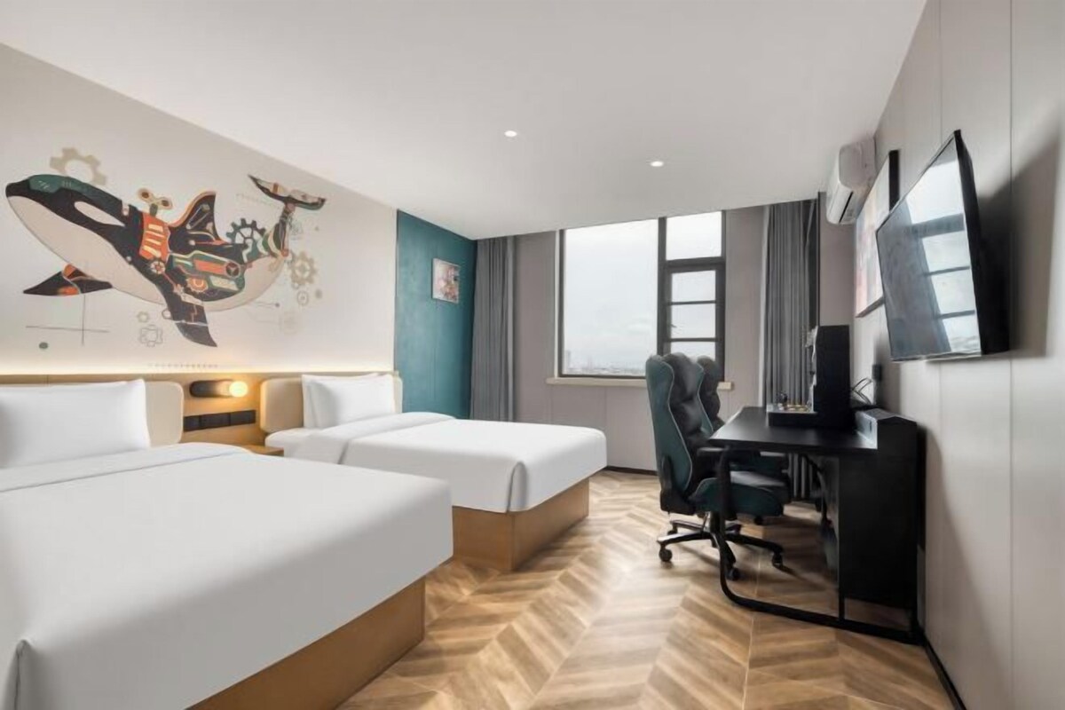 A hotel room with two beds, a desk, a chair, a TV, and a large window.