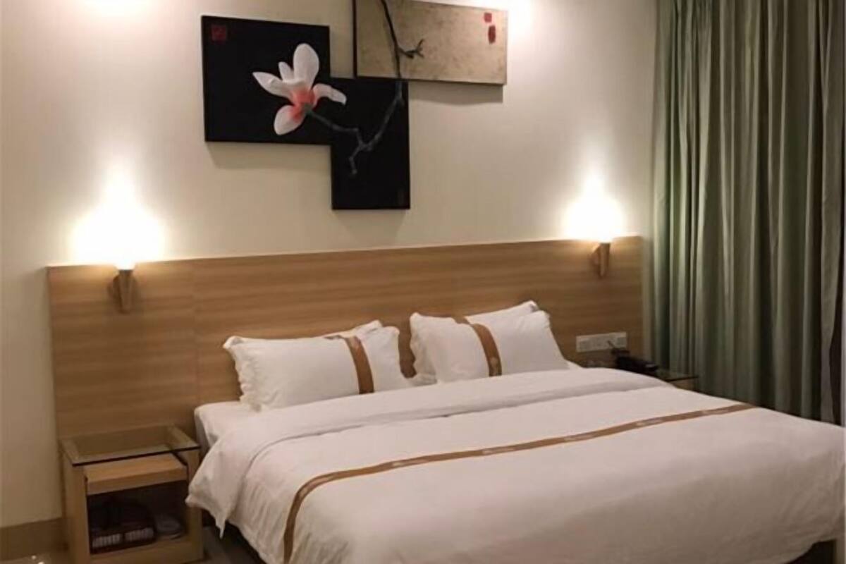 Una habitación de hotel con cabecera de madera, cama con ropa blanca y detalles marrones, una mesita de noche, una lámpara y una obra de arte en la pared.