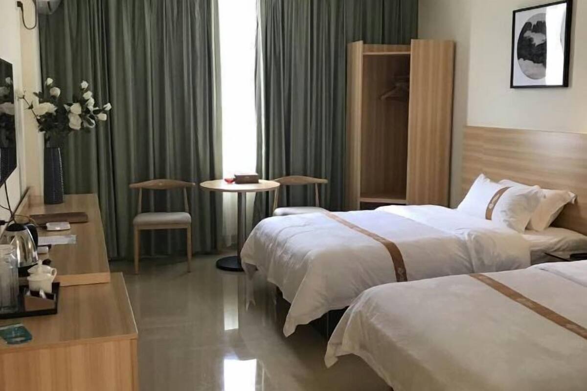 Habitación de hotel con dos camas, un escritorio, una silla, una mesita pequeña y un armario.