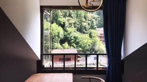Ein Zimmer mit großem Fenster und Blick auf bewaldetes Gebiet, einem Holztisch und einem Stuhl.