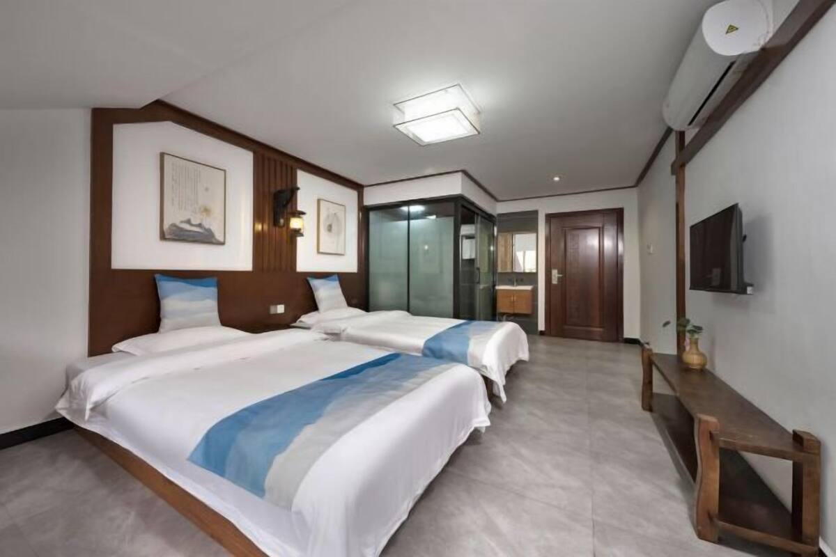Une chambre d’hôtel avec deux lits, un banc en bois, une télévision et un miroir.