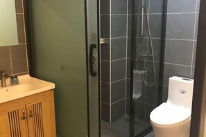 Une salle de bain avec une douche à parois de verre, des toilettes et un meuble-lavabo en bois doté d’un miroir.
