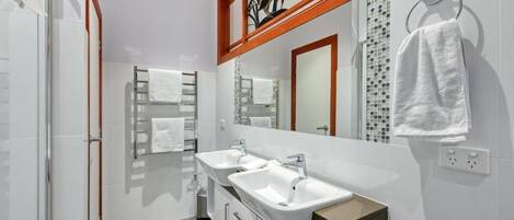 A modern bathroom with two sinks, a large mirror, and a shower area.