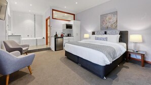 Una habitación de hotel moderna con una cama grande, un área de descanso, una kitchenette y un baño.