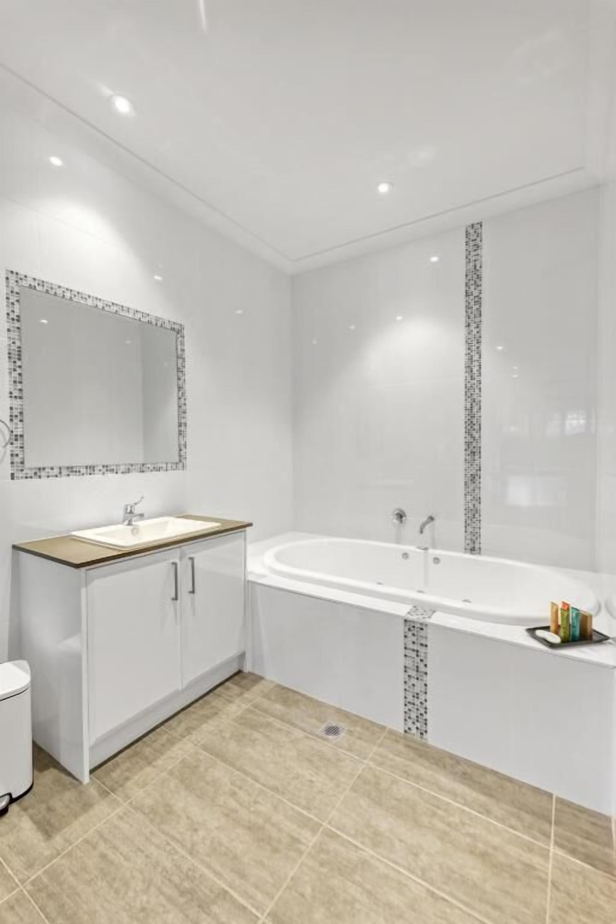 Ein modernes Badezimmer mit einer freistehenden Badewanne, einem großen Spiegel und einem Waschtisch mit Schränken.
