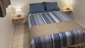 Ein Schlafzimmer mit einem Bett, zwei Nachttischlampen, einem Deckenventilator, einer Wandklimaanlage und einem gewebten Wandbild.
