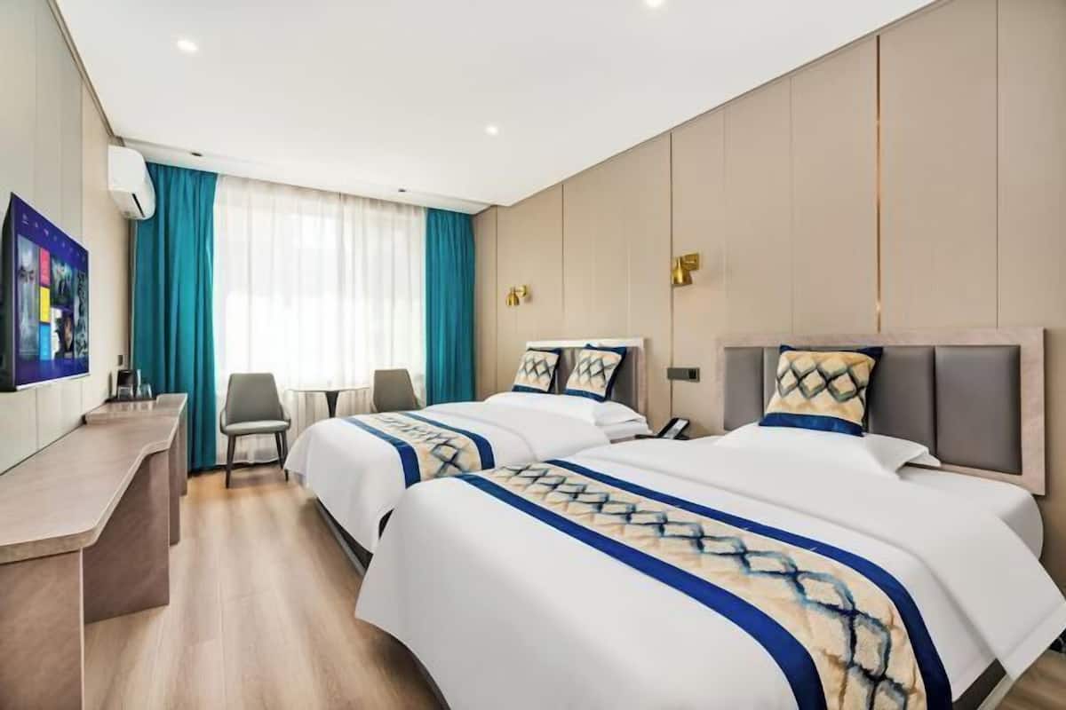 A hotel room with two beds, a desk, a chair, and a TV.