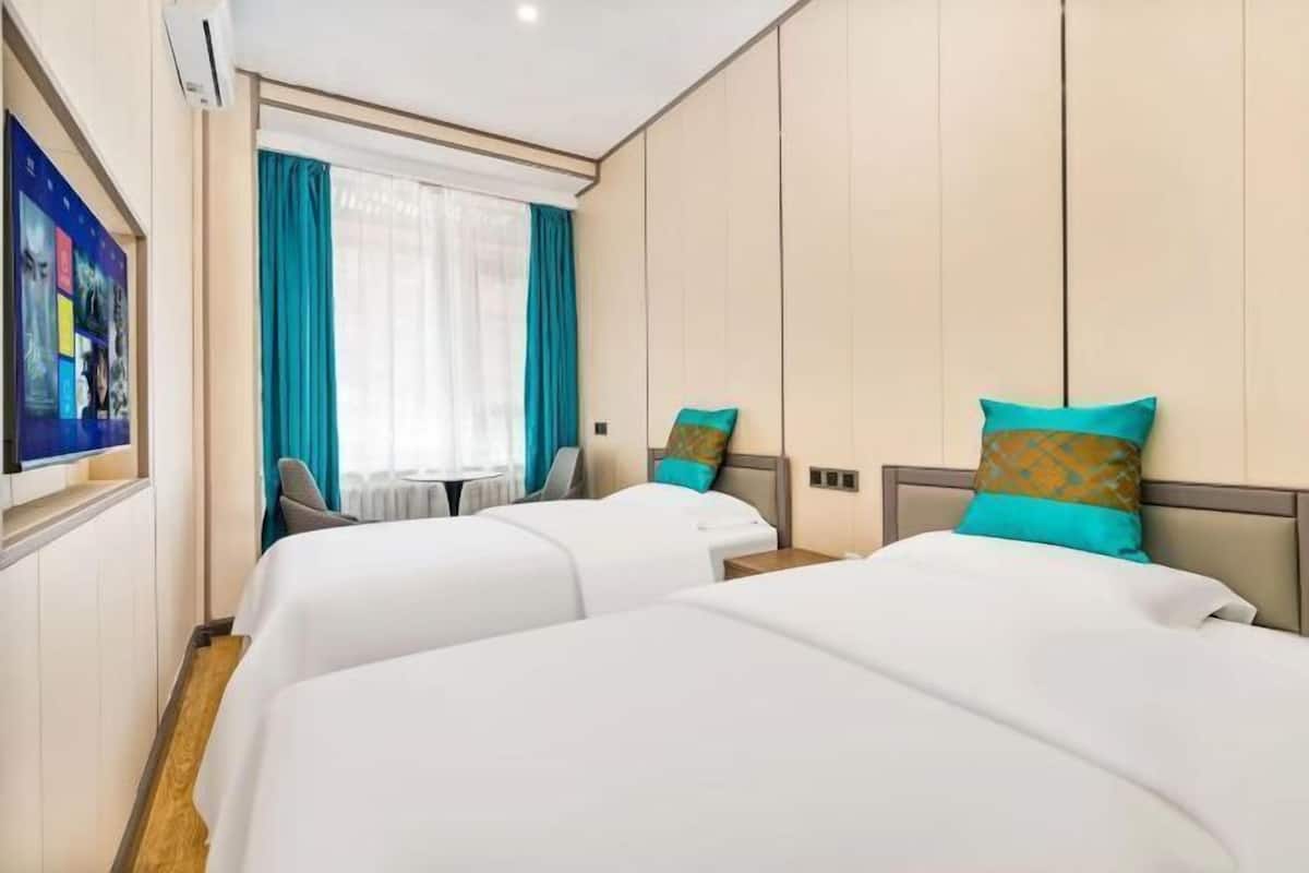 A hotel room with two beds, a desk, and a window with curtains.