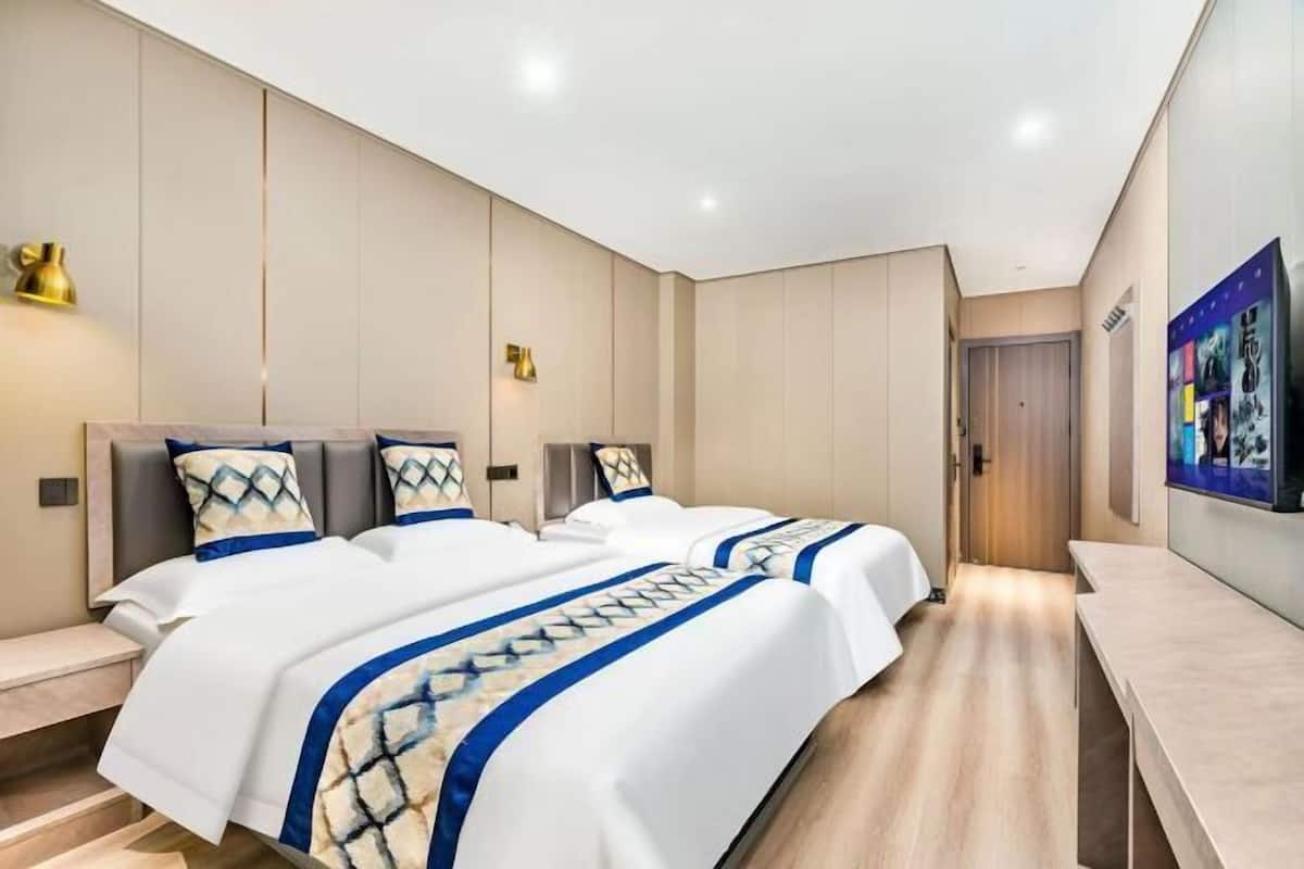 A modern hotel room with two beds, a desk, and a wall-mounted TV.