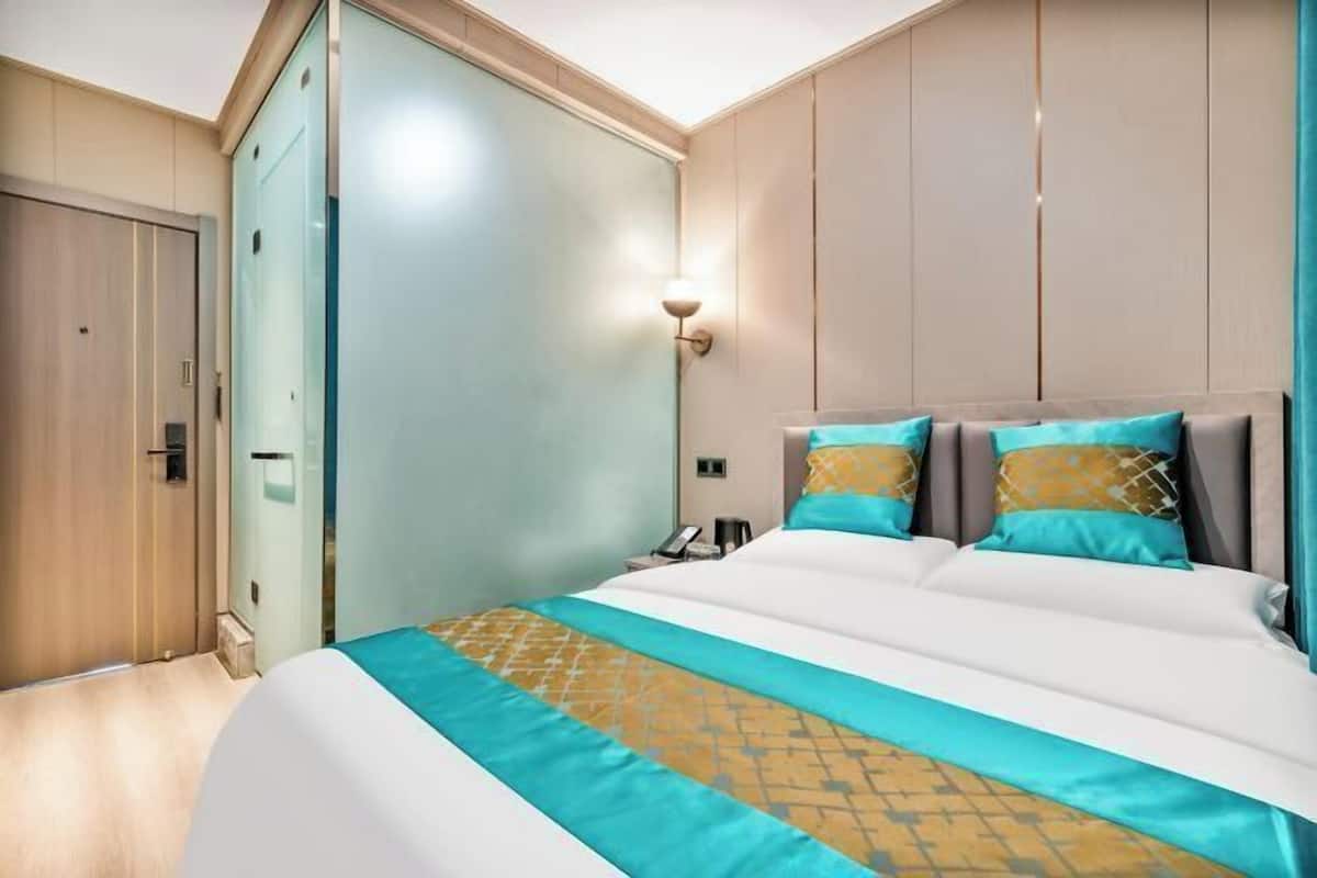 A hotel room with a bed, a wardrobe, a bedside table, and a wall-mounted light.