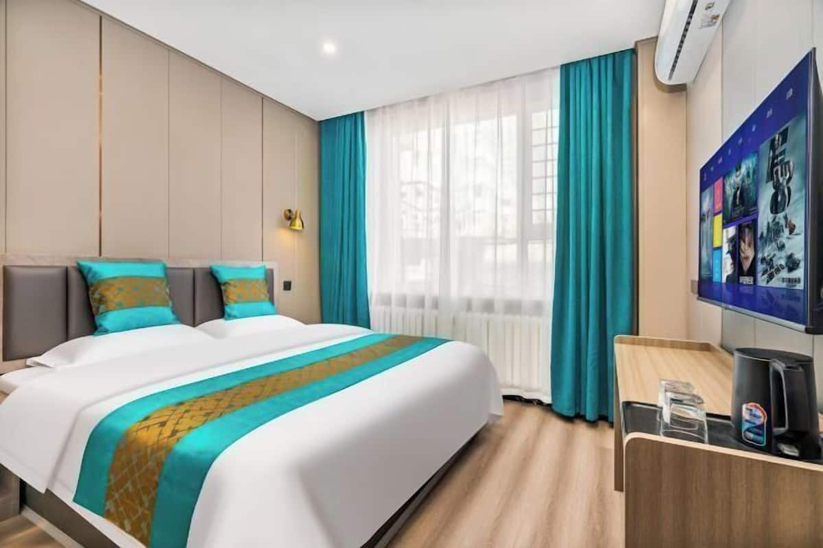 A hotel room with a bed, a desk, a TV, and a window with curtains.