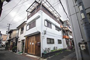A two-story residential building with a wooden front door, a balcony on the upper floor, and a bicycle parked outside. - Miyu・Tsuruhashi Japanese-style house Up to 6 people (Osaka)