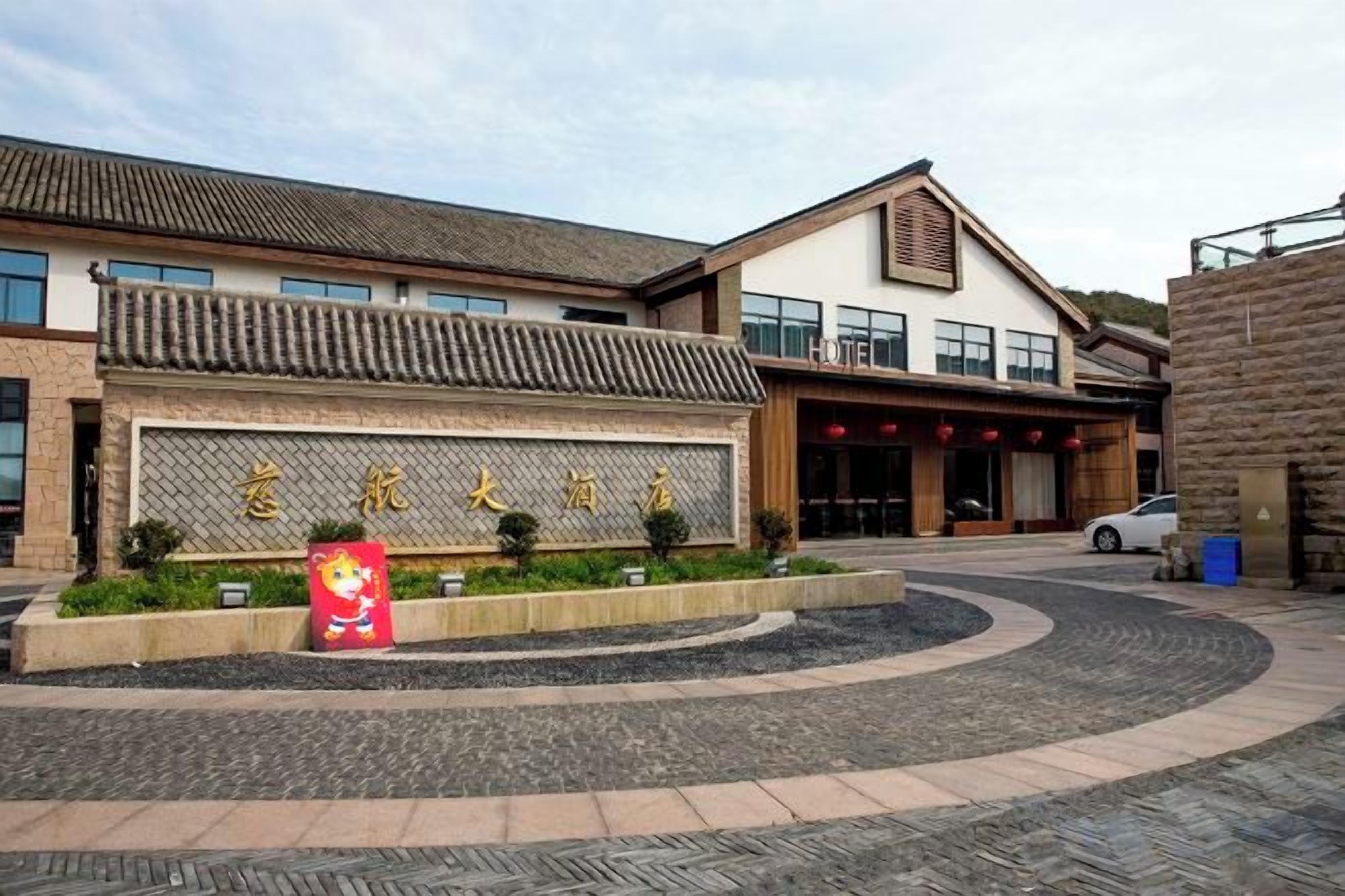 Entrada de un hotel con tejado de baldosas, un gran letrero con caracteres chinos y una estatua de mascota roja.