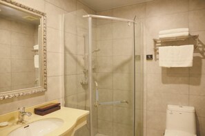 A bathroom with a glass-enclosed shower, a sink with a mirror, and a toilet. - Cihang Hotel (Zhoushan)