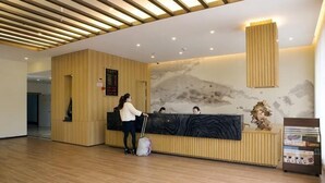 A reception area with a wooden reception desk, a receptionist, and a guest. - Cihang Hotel (Zhoushan)