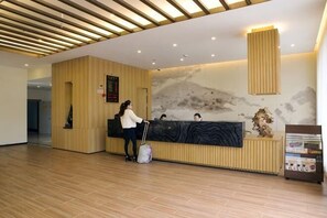 A reception area with a wooden reception desk, a receptionist, and a guest.