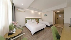 A hotel room with two beds, a small table with a vase of flowers, a green chair, and a wooden desk. - Cihang Hotel (Zhoushan)