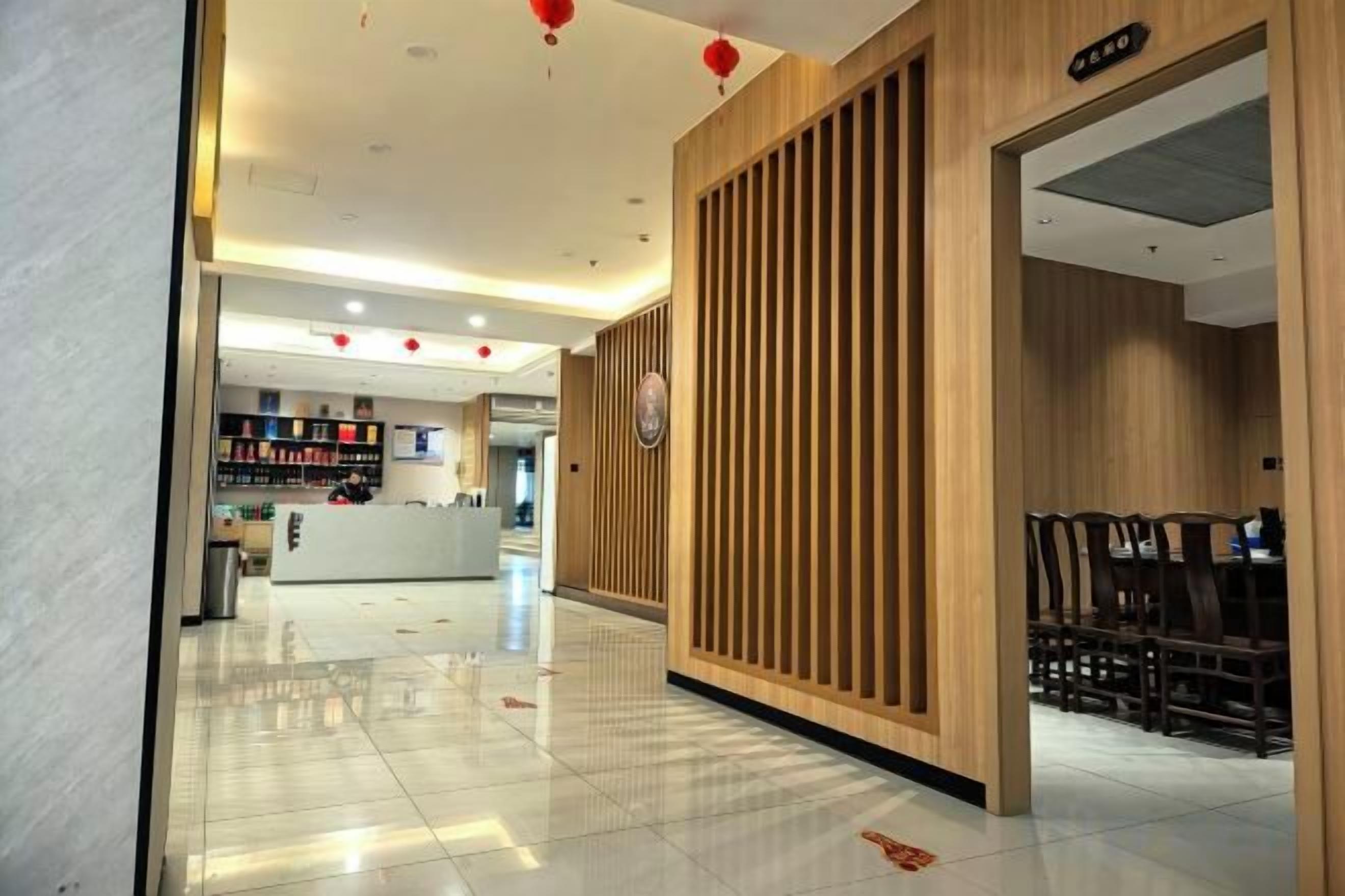 A hotel lobby with a reception desk, a wooden panel wall, and a seating area with tables and chairs.