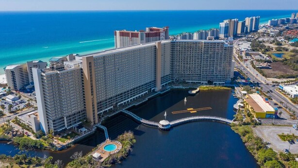 A large hotel complex with multiple high-rise buildings, a central courtyard with a pool, and a view of the ocean.